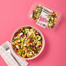 Load image into Gallery viewer, Colourful bean medley salad in a bowl with a container labeled 'Salad Servers' on a pink background.