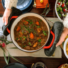 Load image into Gallery viewer, Person holding a pot of stew with vegetables on a table with other dishes.