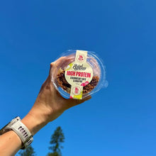Load image into Gallery viewer, A hand holding a clear plastic tub of Salad Servers High Protein Chia against a bright blue sky background.