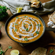 Load image into Gallery viewer, bowl of orange soup with a swirl of white cream, garnished with green herbs, on a wooden table.