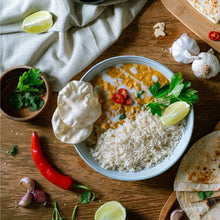 Load image into Gallery viewer, bowl of rice with a yellow sauce, garnished with herbs and lime, on a wooden table.