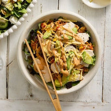 Load image into Gallery viewer, Salad with chicken, vegetables, and a dressing in a bowl on a wooden table.