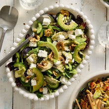 Load image into Gallery viewer, Green salad with avocados, cucumbers, and feta cheese in a white bowl on a wooden surface.