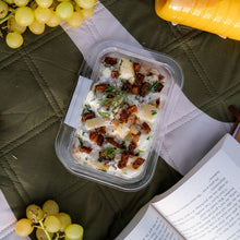 Load image into Gallery viewer, Container of salad with nuts and herbs on a green surface with grapes and a book.