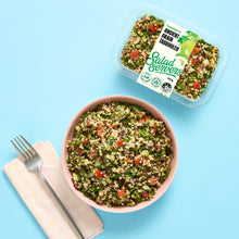 Load image into Gallery viewer, A pink bowl filled with mixed grain tabouleh salad is shown on a light blue background, alongside a clear plastic container of the same salad and a fork on a napkin. The label on the container reads Salad Servers.