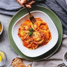 Load image into Gallery viewer, Ravioli with Basilico sauce topped with fresh parsley and parmesan cheese on a white square plate