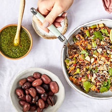 Load image into Gallery viewer, Japanese Sesame Rice Salad with Honey & Edamame in a bowl on a table with a small bowl of olives and a bowl of dressing
