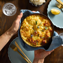 Load image into Gallery viewer, Potato Bake in a round black baking dish garnished with fresh rosemary