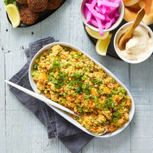Load image into Gallery viewer, A white serving tray of Pumpkin Cous Cous with falafels, pickles, hummus and lemon on the side on white wooden background.