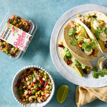 Load image into Gallery viewer, A plate of tacos filled with Bean Medley with Lemon Zest, avocado and coriander on a white plate. A bowl and plastic container of bean medley nearby on a blue background.