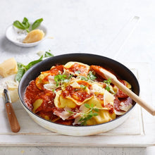 Load image into Gallery viewer, A bowl filled with Spinach and Ricotta ravioli and a wooden serving spoon resting on top. A knife and wedge of parmesan sits off to the side.