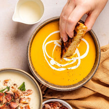Load image into Gallery viewer, Pumpkin Soup with a hand dunking crusty bread into it