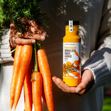 Load image into Gallery viewer, A person in a gray knit sweater holds a bottle of Salad Servers Japanese Style Garrot & Ginger dressing in one hand and a bunch of fresh carrots in the other. The bottle has a white label with orange graphics and a black cap.