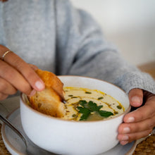 Load image into Gallery viewer, Person dipping bread into a bowl of creamy pumpkin soup garnished with herbs and seeds.