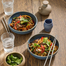 Load image into Gallery viewer, Two bowls of noodles with vegetables and meat on a wooden table with glasses of water and a small pitcher.

