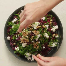 Load image into Gallery viewer, Person adding ingredients to a salad on a black plate
