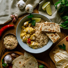 Load image into Gallery viewer, Satay Chicken with naan bread on a wooden table with garnishes
