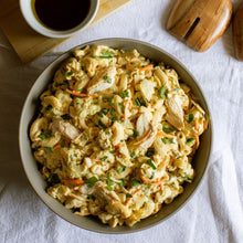 Load image into Gallery viewer, Grey bowl with pasta salad on a white table cloth with oil and salad servers
