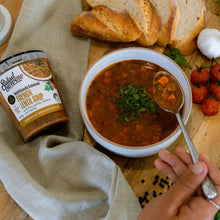 Load image into Gallery viewer, Bowl of French lentil soup with herbs, bread, tomatoes, and packaged soup tub on a wooden table.
