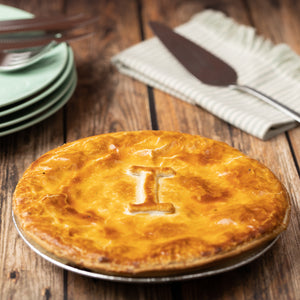 Baked Aussie Beef pie on a wooden table with plates and a knife in the background