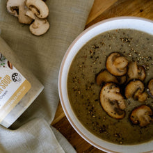 Load image into Gallery viewer, Bowl of creamy mushroom soup topped with sliced mushrooms and pepper, with packaged soup tub beside it.
