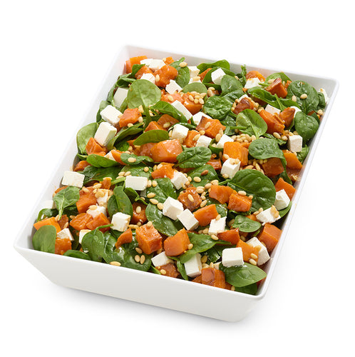 Salad with spinach, sweet potatoes, and feta cheese in a white bowl on a white background