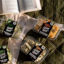 Load image into Gallery viewer, Plastic containers of 'Lunch Rush' salads on a textured surface with an open book.
