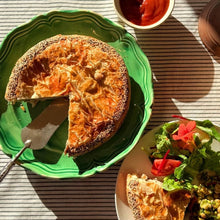 Load image into Gallery viewer, Pie with a slice removed on a green plate, accompanied by a salad and ketchup on a striped tablecloth.
