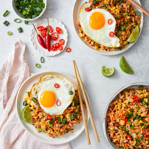 Two plates of fried rice with eggs and vegetables on a light gray surface.