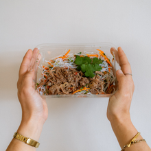 Load image into Gallery viewer, Hands holding a clear container of Thai beef vermicelli salad.
