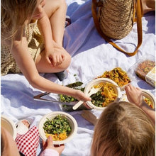 Load image into Gallery viewer, Two children eating outdoors on a white blanket with food and a bag.
