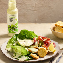 Load image into Gallery viewer, A plated Salad Dressing product presentation featuring a bottle of Salad Servers Herry Caesar dressing alongside a fresh salad with lettuce, cheese, bacon, croutons, and lemon on a plate, with a bowl of croutons in the background.
